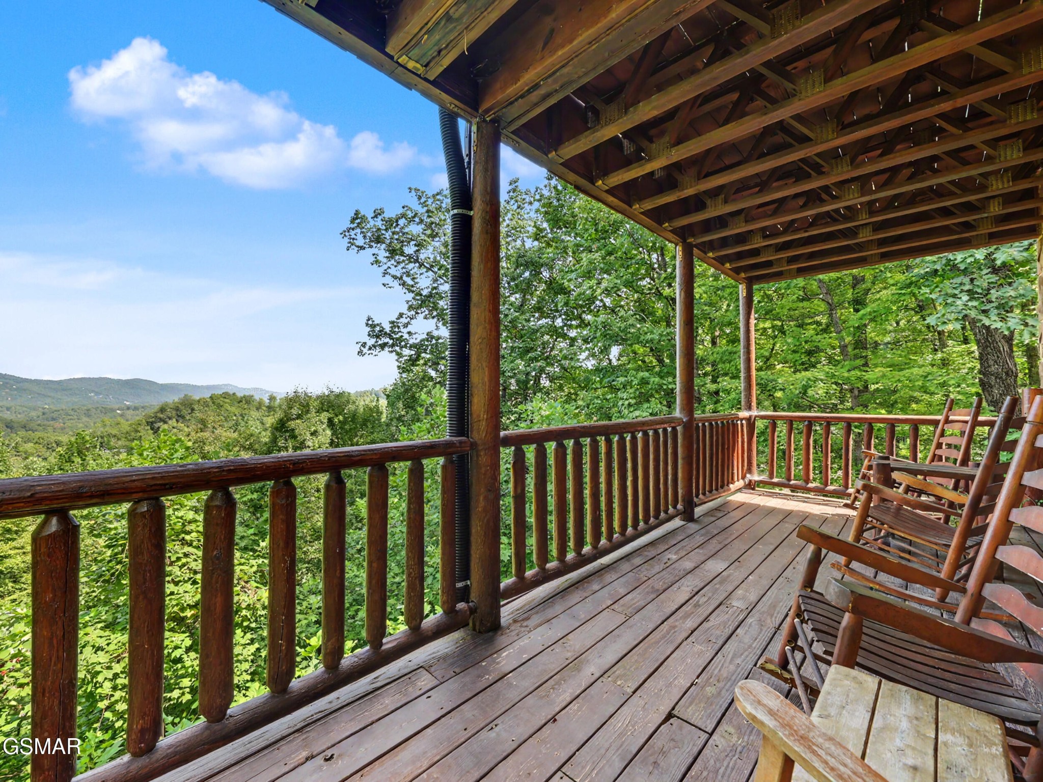 Covered wooden porch with rocking chairs overlooking forested mountains.