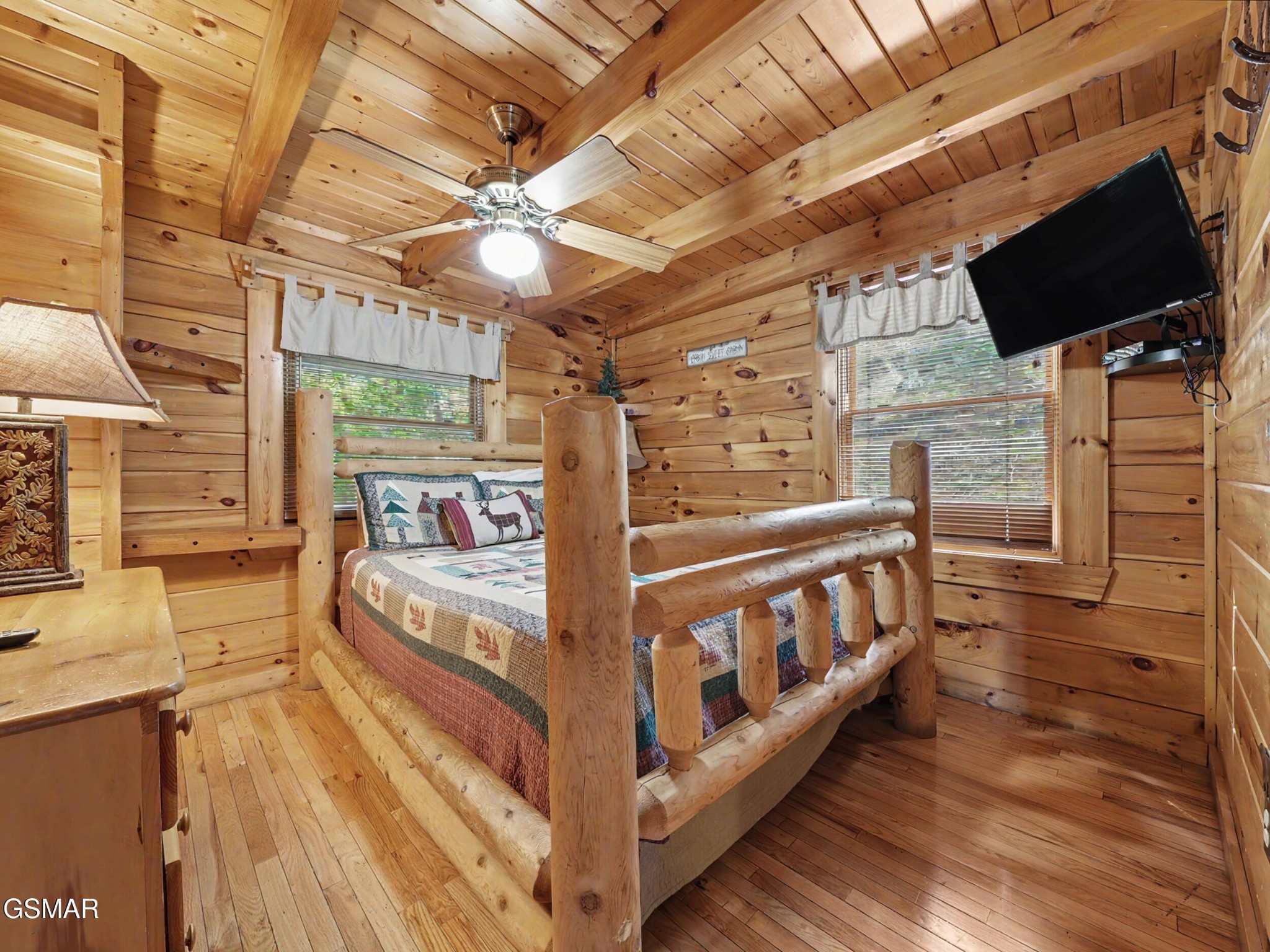 Rustic log cabin bedroom with a log-frame bed, patchwork quilt, and wall-mounted television.