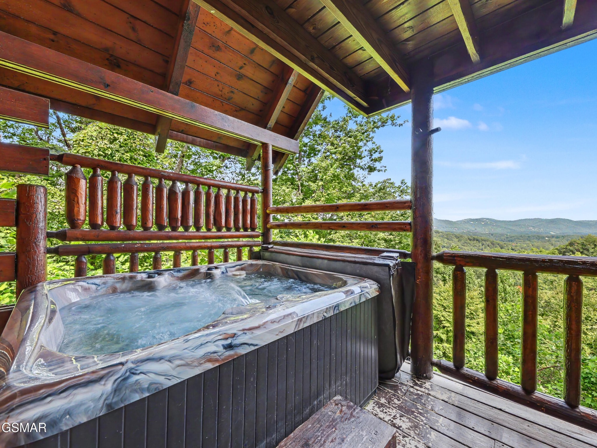 Outdoor hot tub on a covered wooden deck overlooking green mountain ridges.