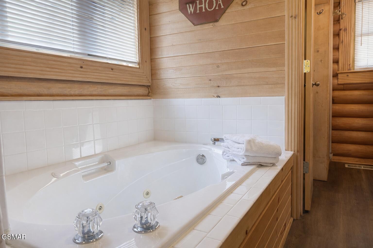 Jetted soaking tub with white tile surround, wood-paneled walls, and folded towels.