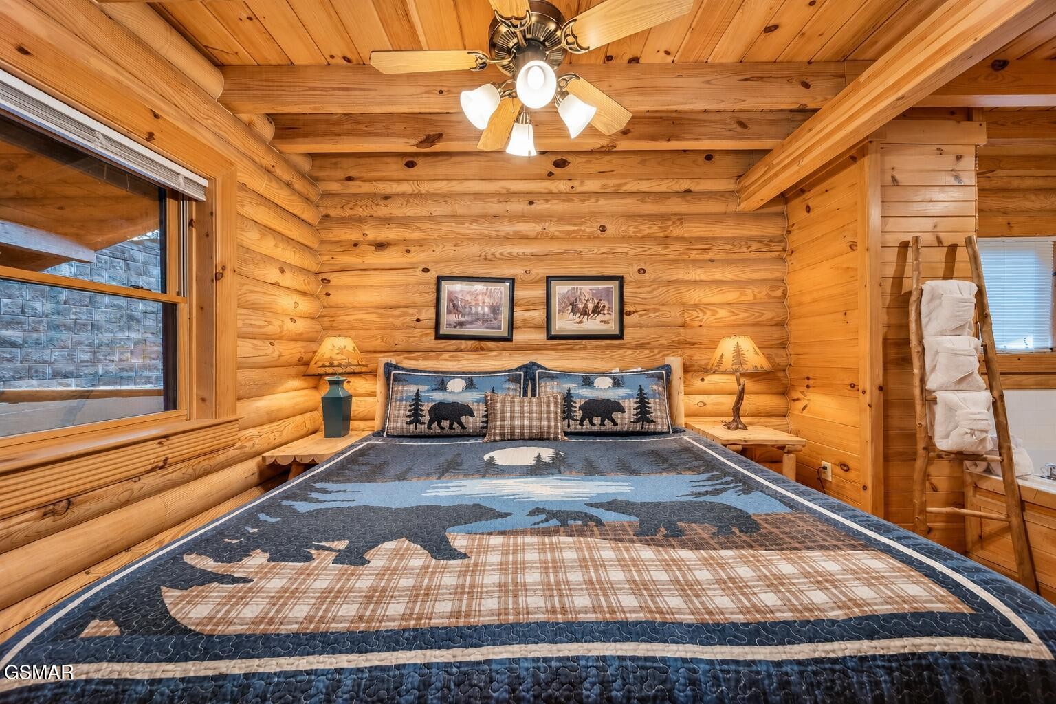 Log cabin bedroom with a bear-pattern quilt, log walls, and framed wildlife prints above the bed.