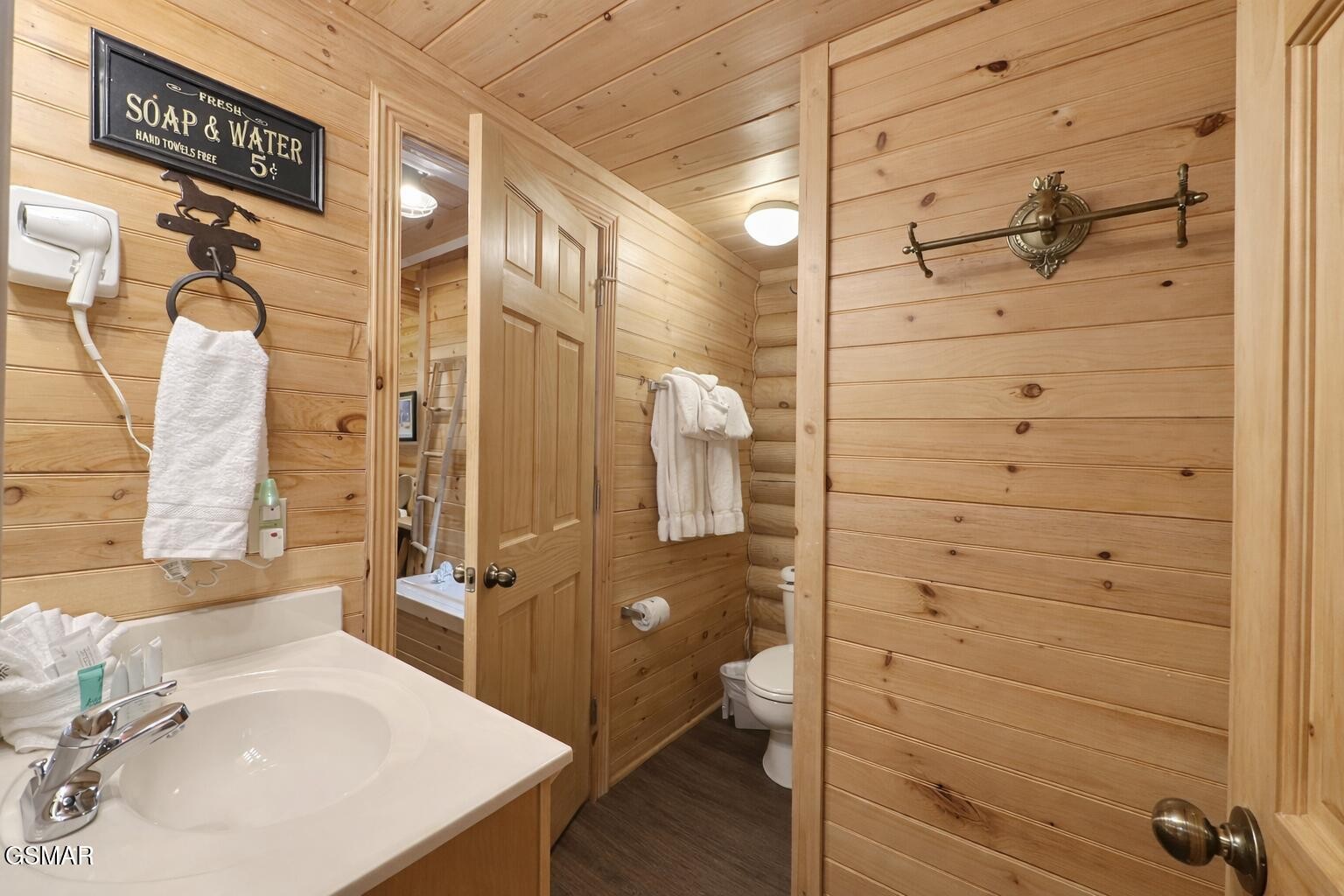 Cabin-style bathroom with wood-paneled walls, white vanity, toilet, and towels.