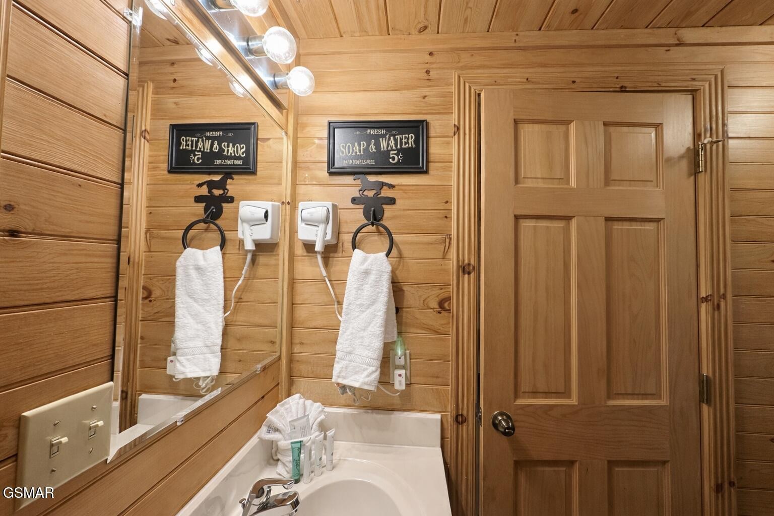 Wood-paneled bathroom with a bathtub, large mirror, white towels, and wall-mounted hair dryers.