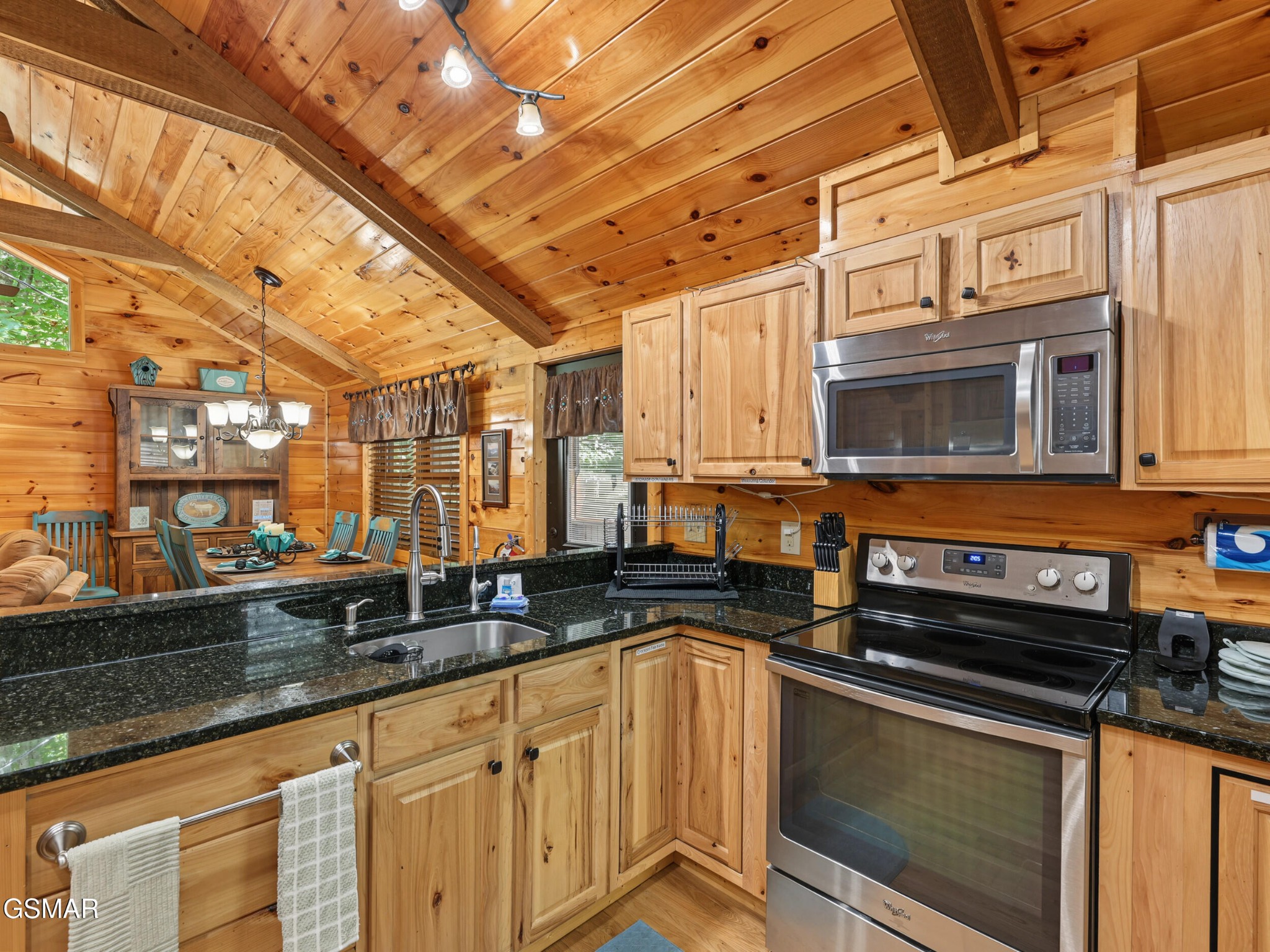 Log-cabin kitchen with a vaulted wood ceiling, black granite counters, and stainless-steel appliances.