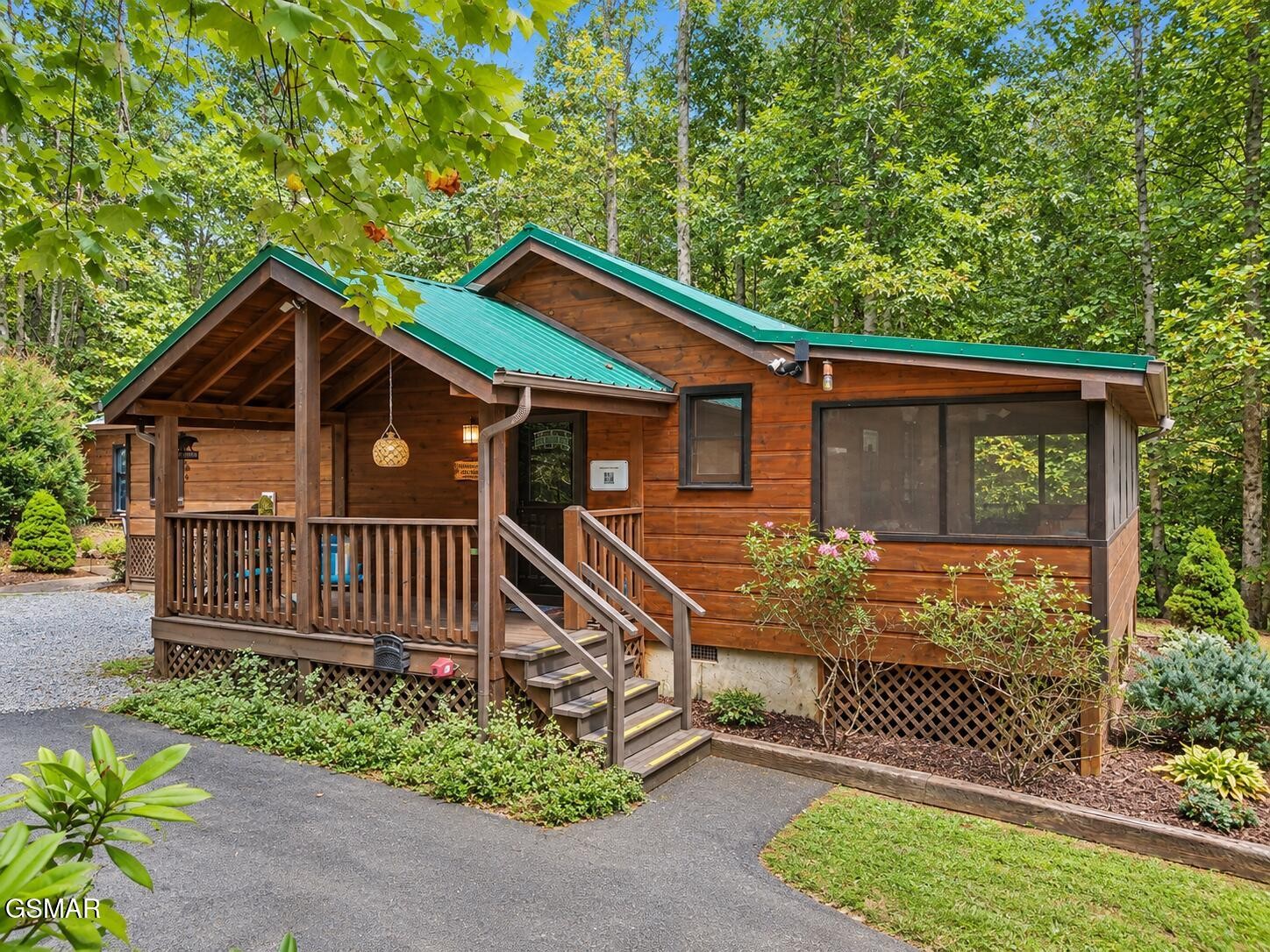 Wood-sided cabin with a green metal roof, covered porch, and screened-in porch among trees.