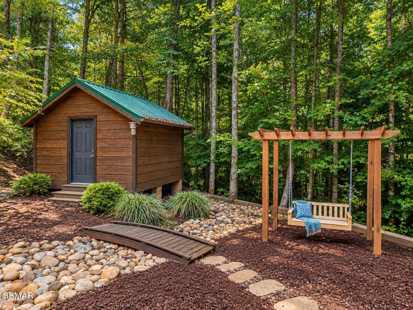 Wooded backyard with a small wooden shed, stone landscaping, and a pergola swing.