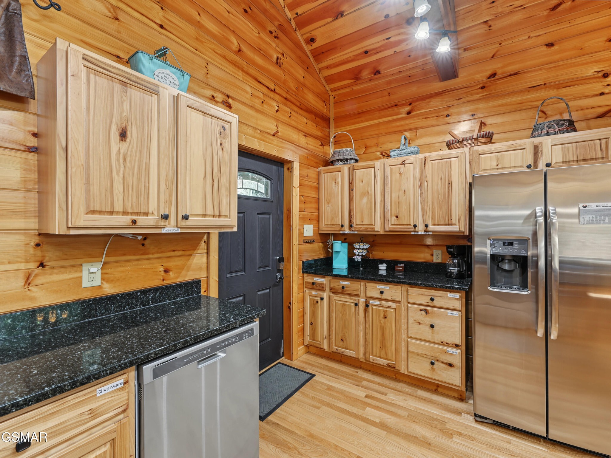 Cabin kitchen with knotty wood cabinets, black granite counters, and stainless steel appliances.