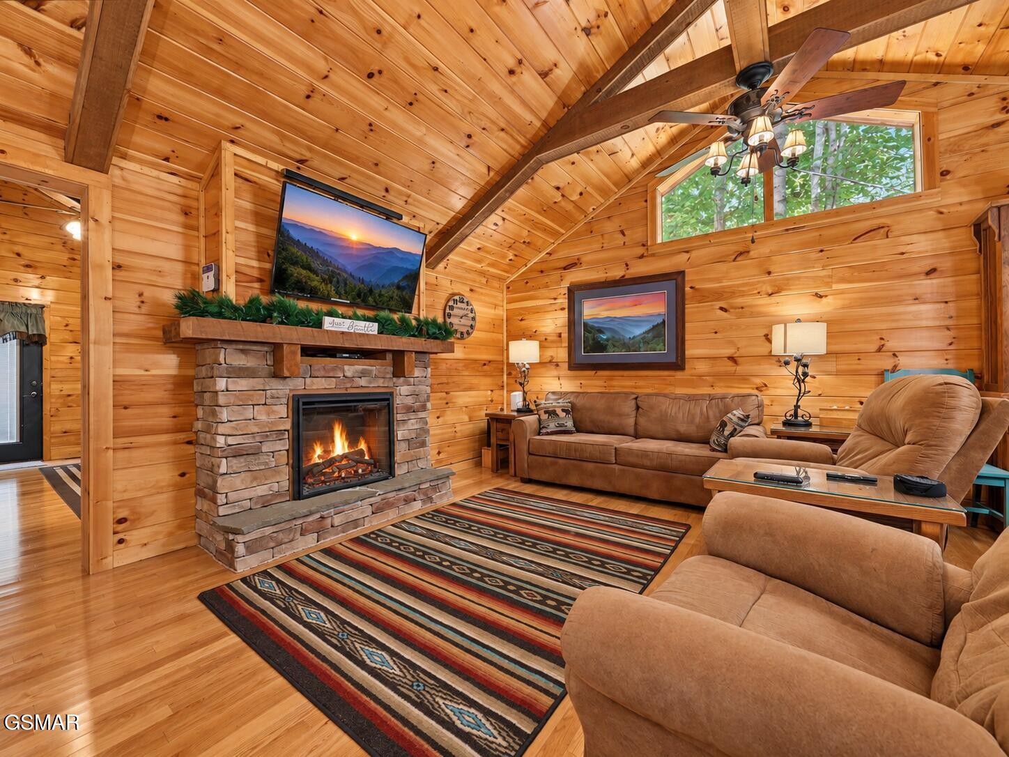 Cabin living room with a vaulted wood ceiling, stone fireplace, and leather seating.
