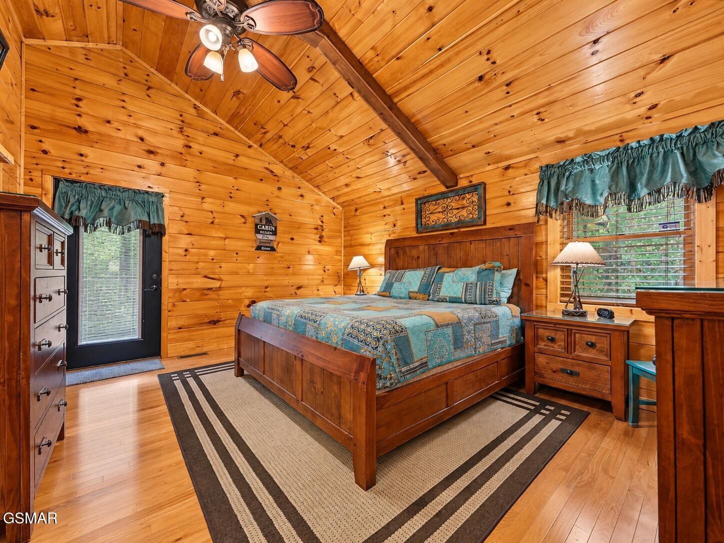 Cabin bedroom with a wooden bed, blue patterned bedding, and vaulted knotty-pine ceiling.