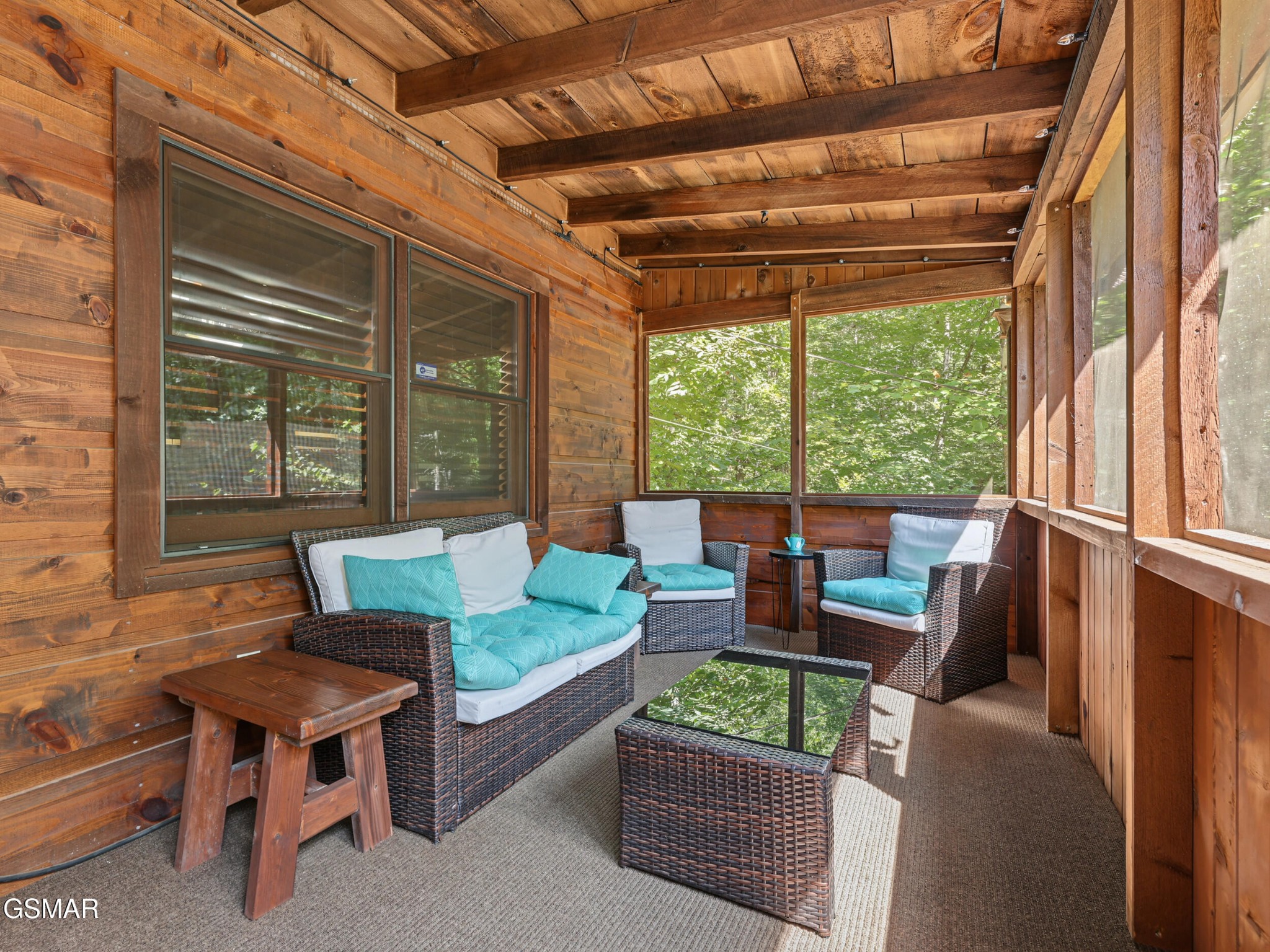 Screened porch with timber walls, wicker seating, turquoise cushions, and leafy views.