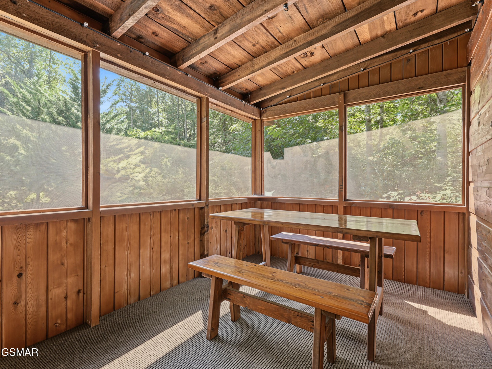 Screened wooden porch with a picnic table and leafy woods visible through the windows.