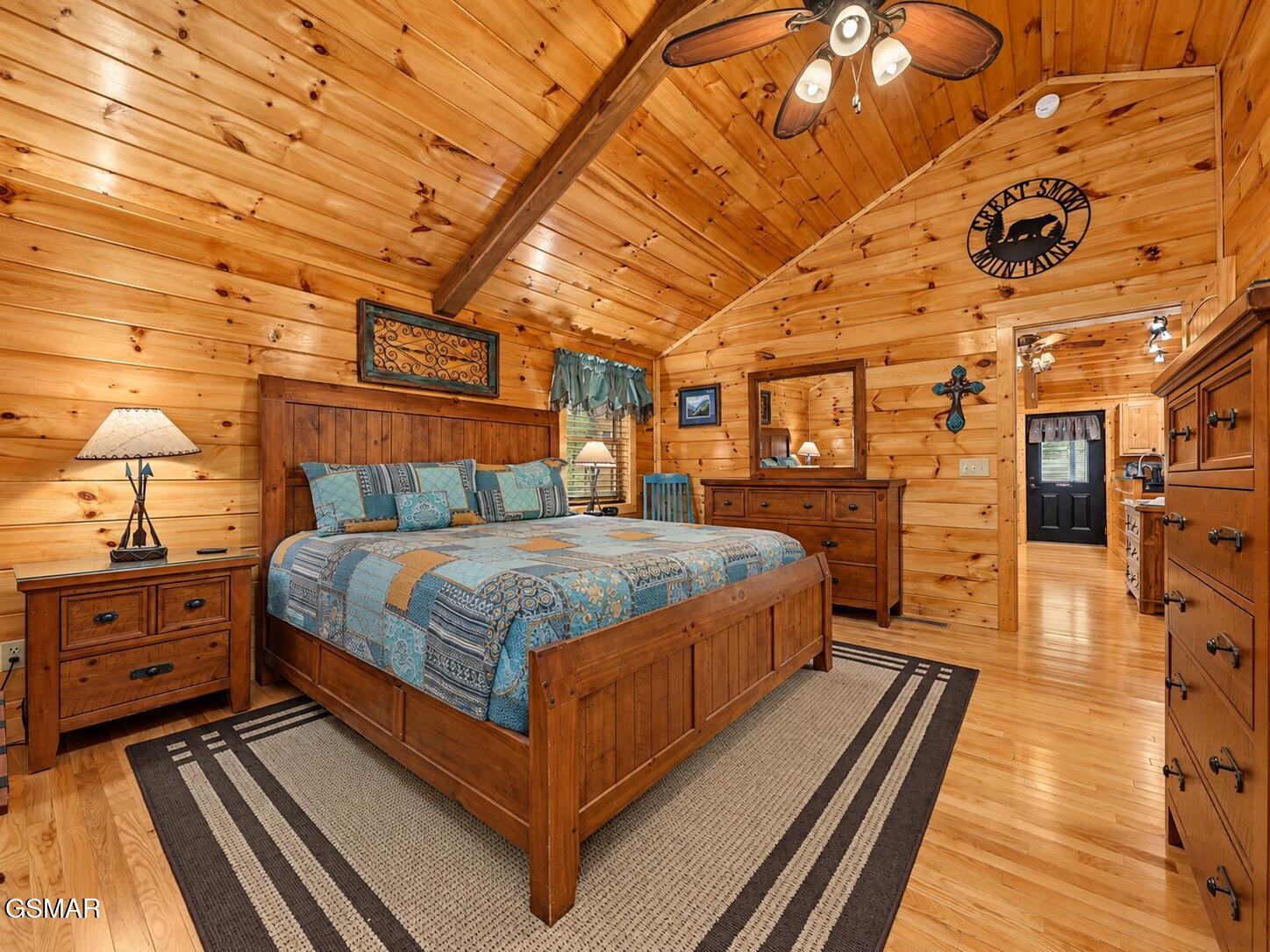 Cabin bedroom with a wooden bed, blue patterned bedding, and knotty pine walls and vaulted ceiling.
