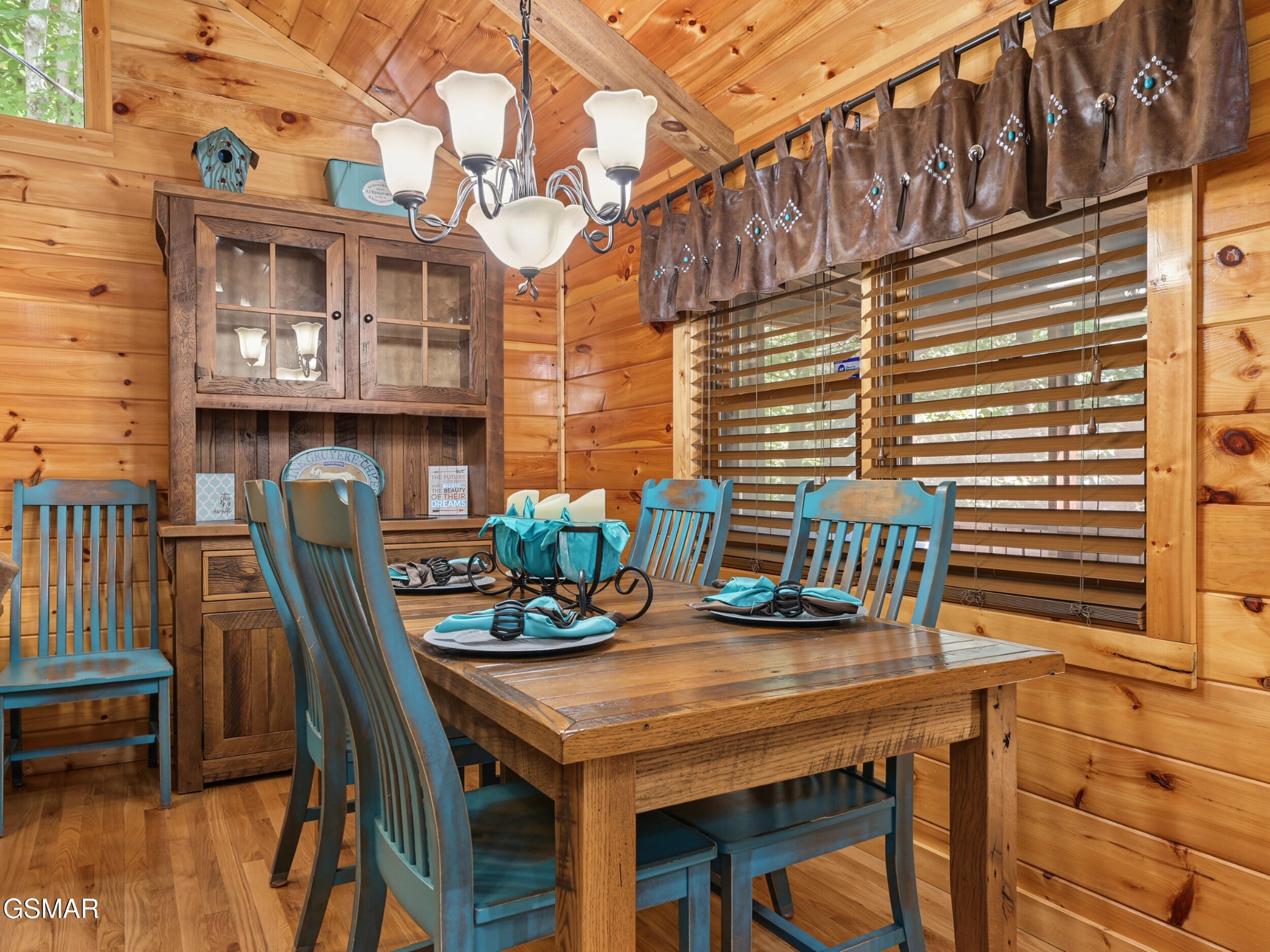Cabin dining room with a rustic wood table, turquoise chairs, and knotty pine walls.