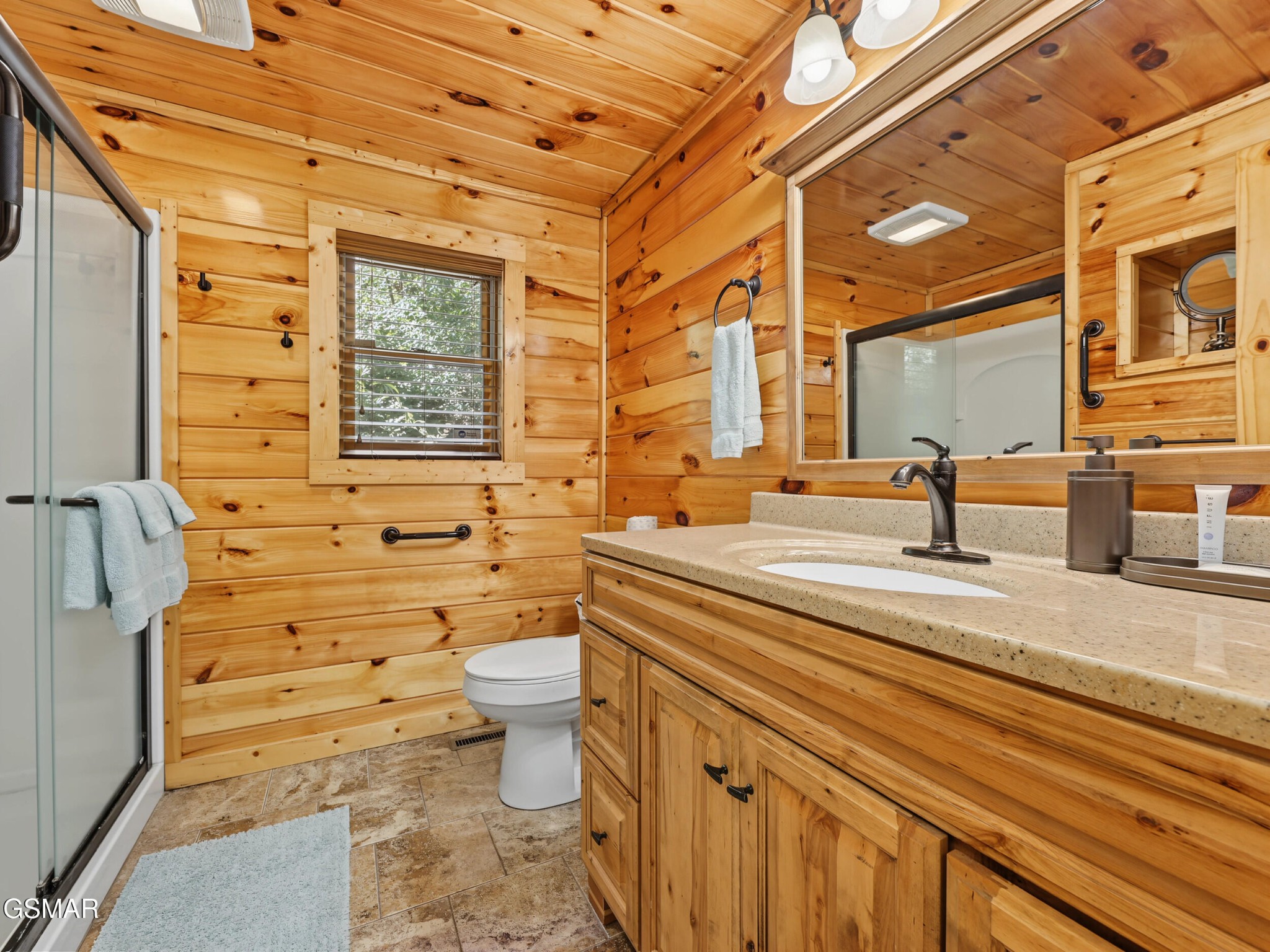 Cabin bathroom with knotty-pine walls, glass shower, and a long wood vanity.
