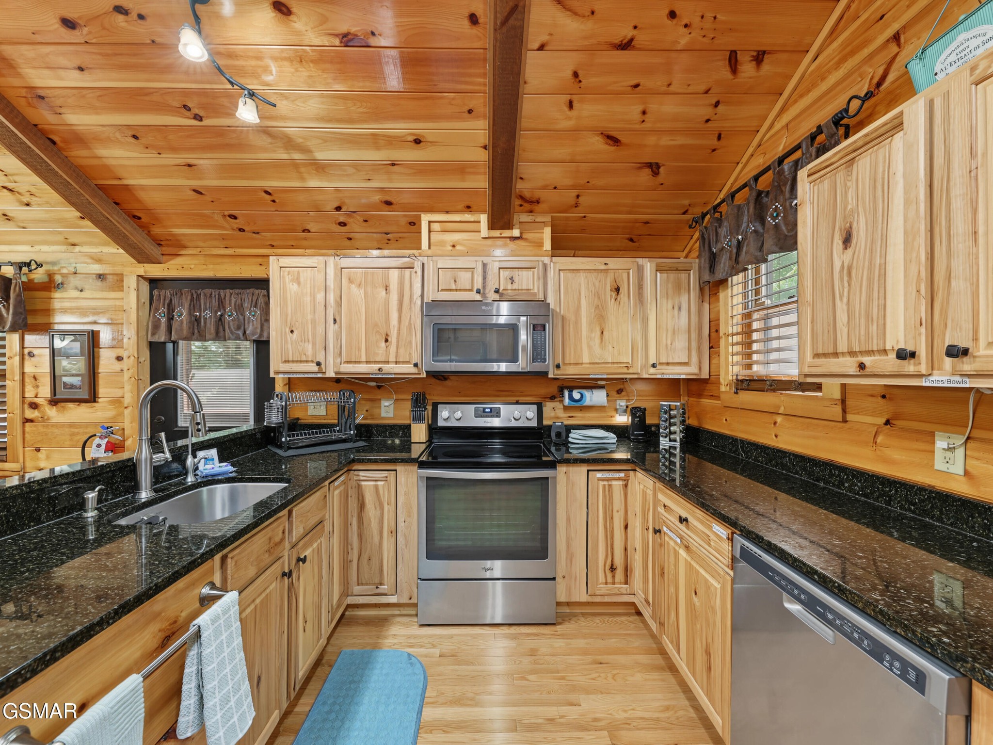 Log-cabin kitchen with knotty wood cabinetry, black granite counters, and stainless-steel appliances.