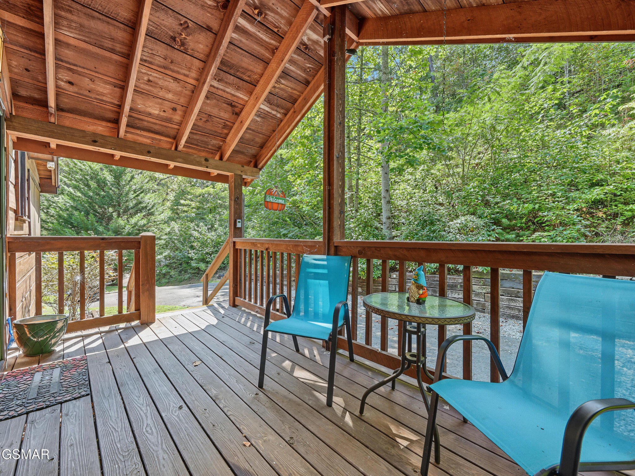 Covered wooden porch with blue chairs and a table overlooking dense green woods.