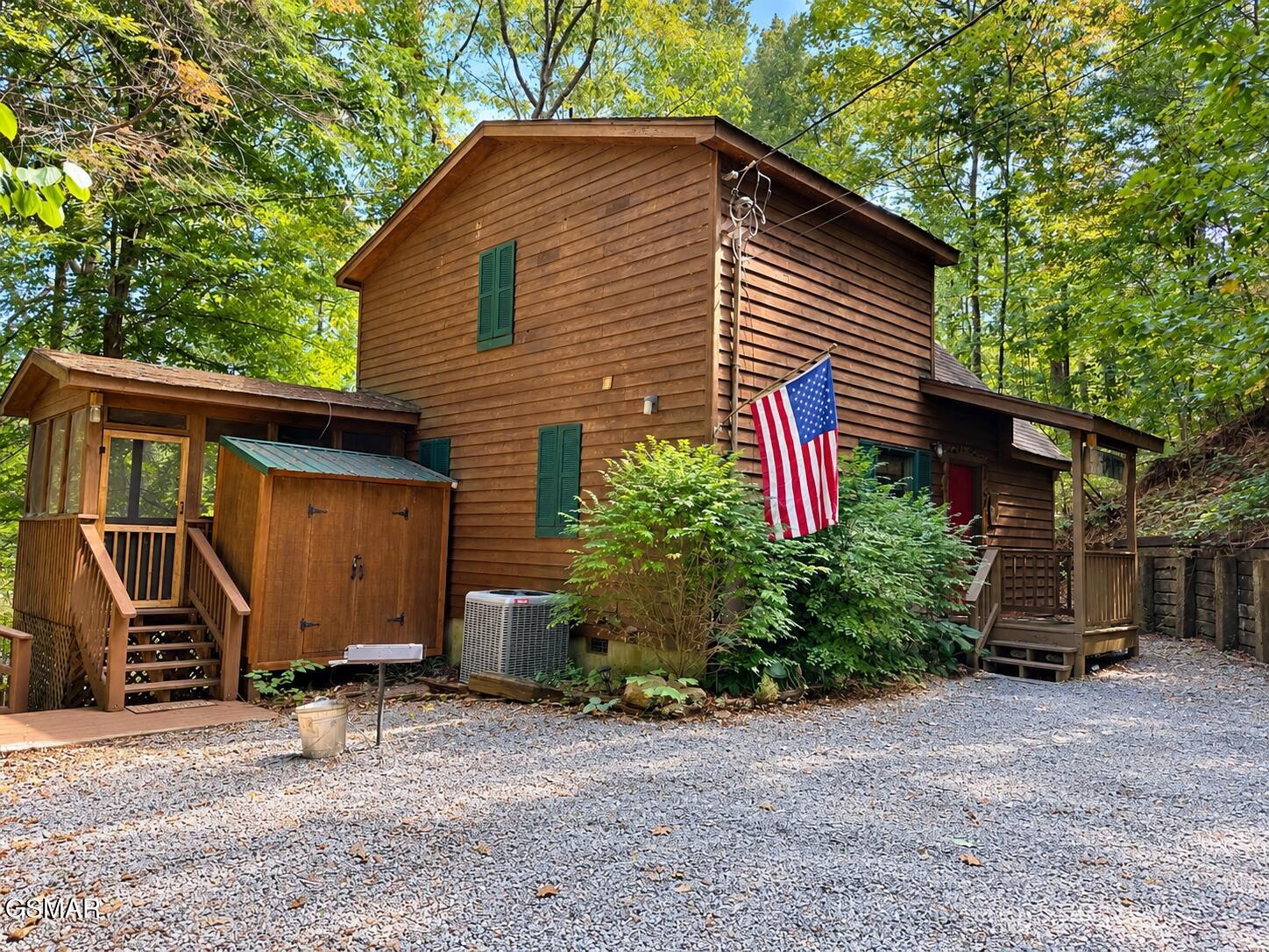 Wood-sided cabin with covered porches and an American flag in a wooded setting.