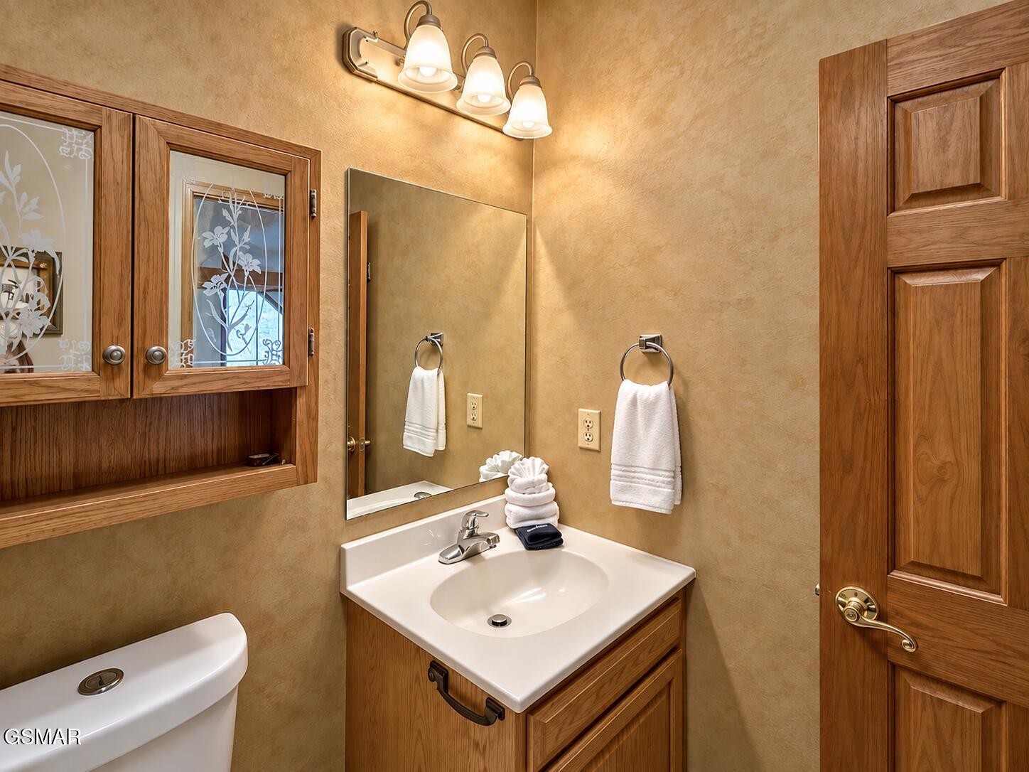 Bathroom with a wood vanity, mirrored cabinet, white sink, and paneled wooden door.