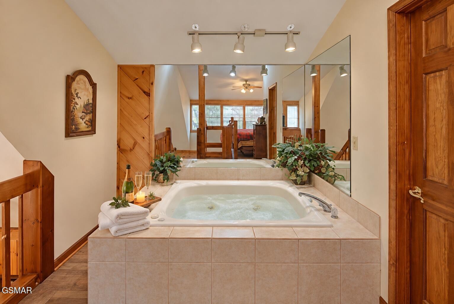 Tiled bathroom with an illuminated jetted tub, large mirror, and warm wood trim.