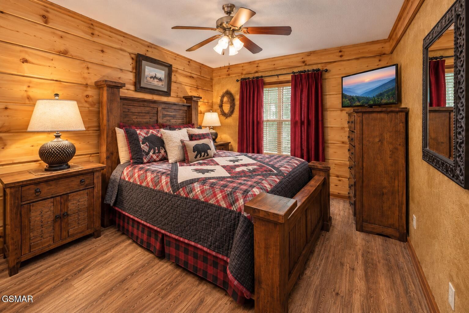 Rustic bedroom with plaid bedding, knotty wood walls, and red curtains.
