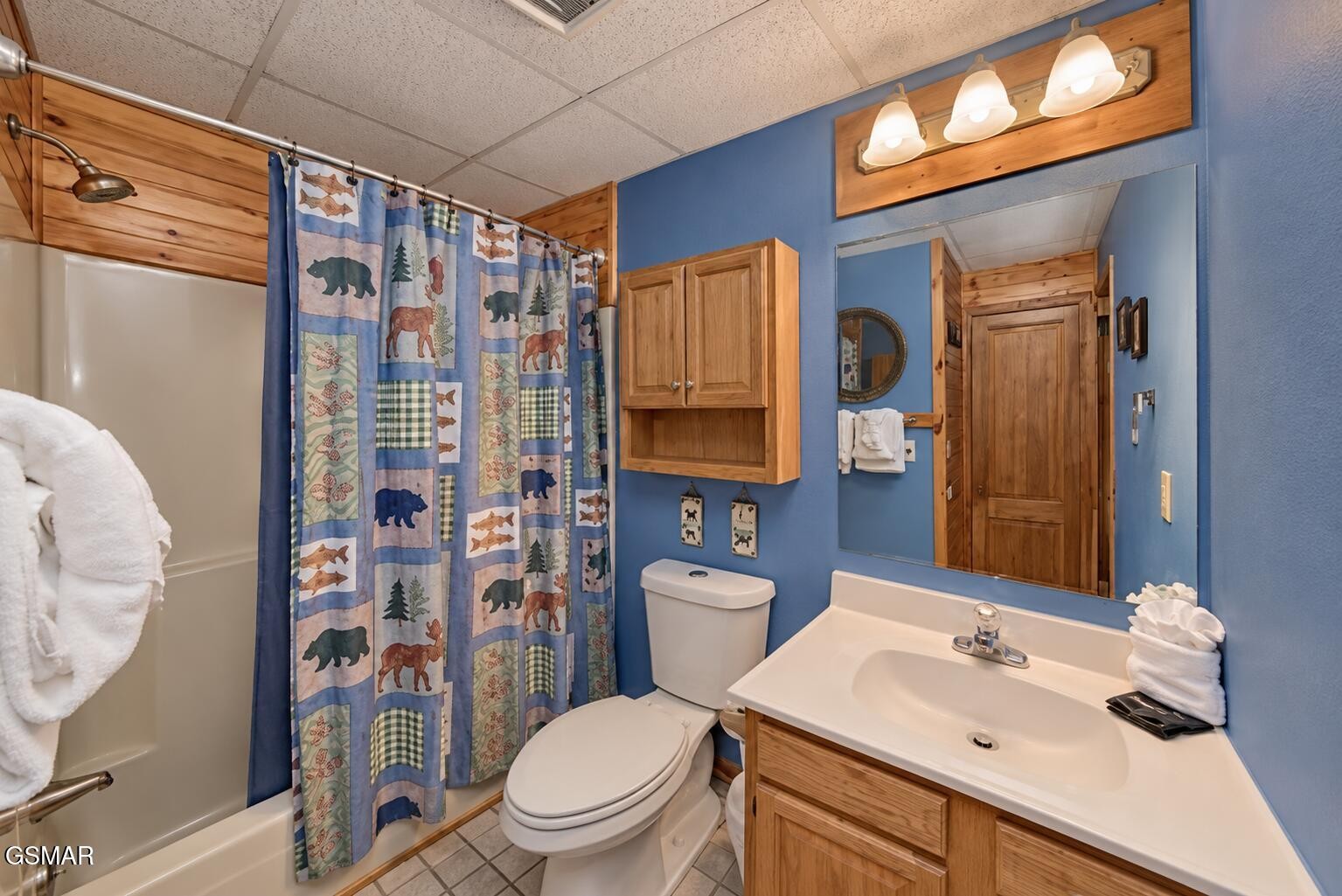 Bathroom with a wildlife-print shower curtain, blue walls, and a wood vanity.