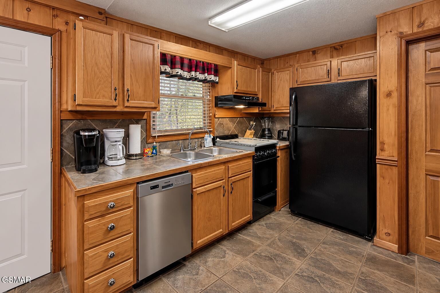 Kitchen with wood cabinets, black appliances, and a double-basin sink beneath a window.