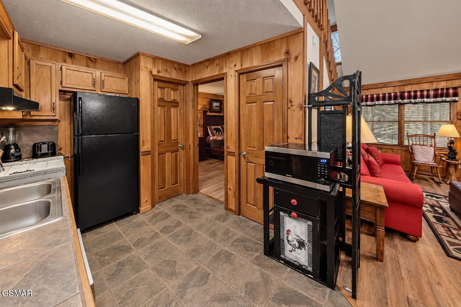 Knotty-pine kitchen with black appliances opening onto a living area with a red sofa.