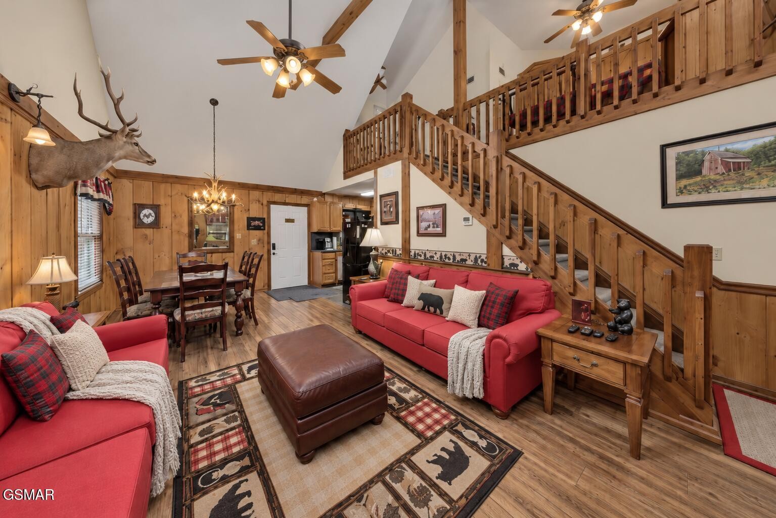 Cabin living room with red sofas, wood-paneled walls, and a staircase leading to an open loft.