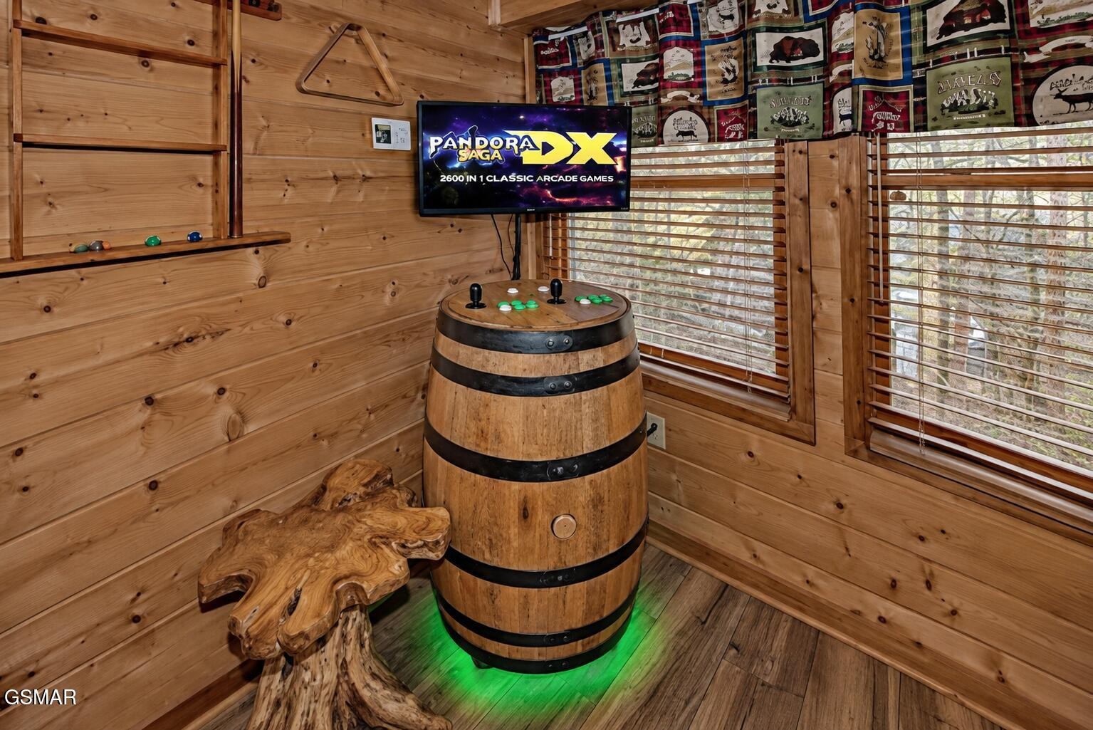 Wood-paneled game room with a barrel-style arcade cabinet, wall-mounted screen, and woodland-print curtains.