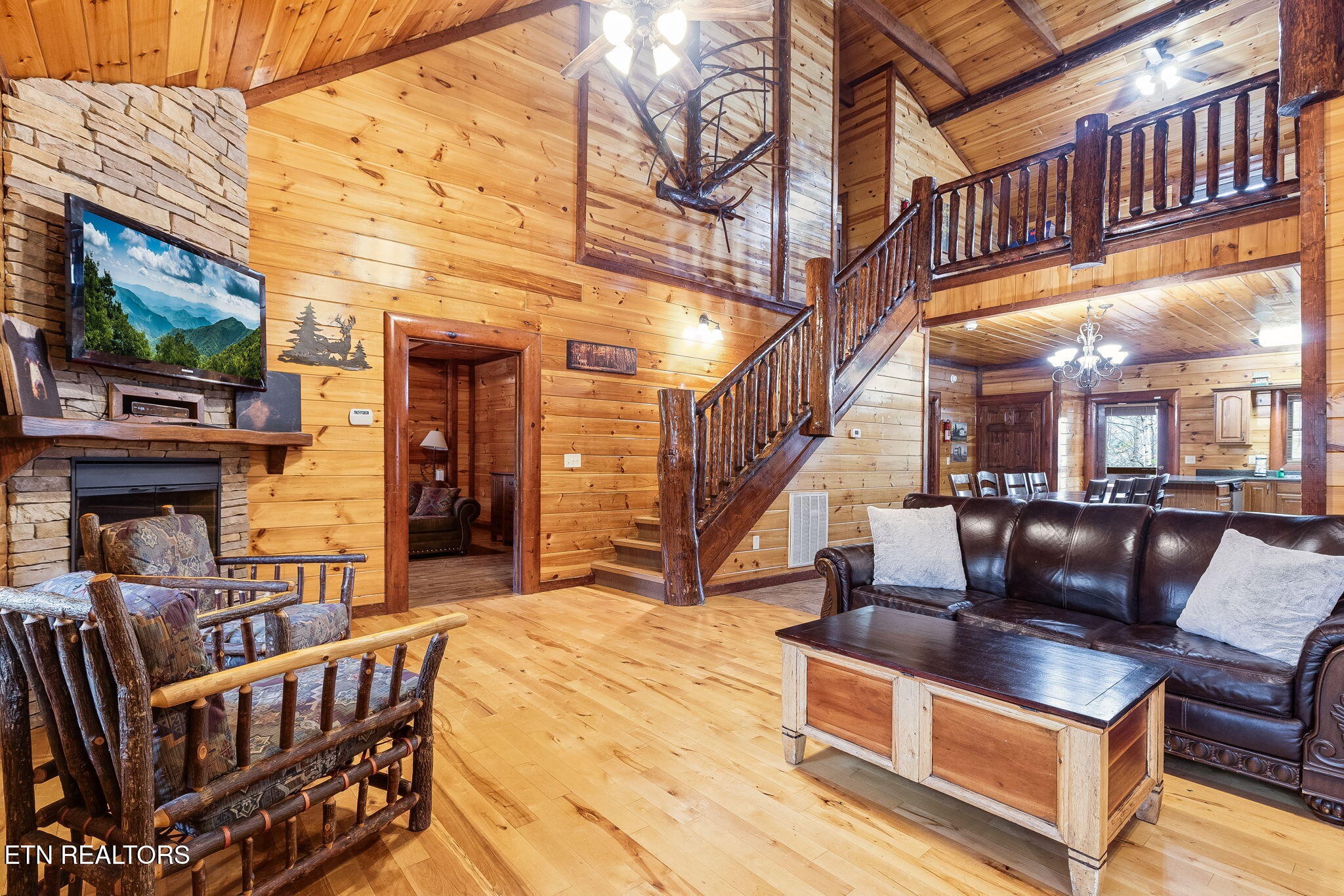 Log cabin living room with a stone fireplace, rustic furnishings, and an open staircase to the loft.