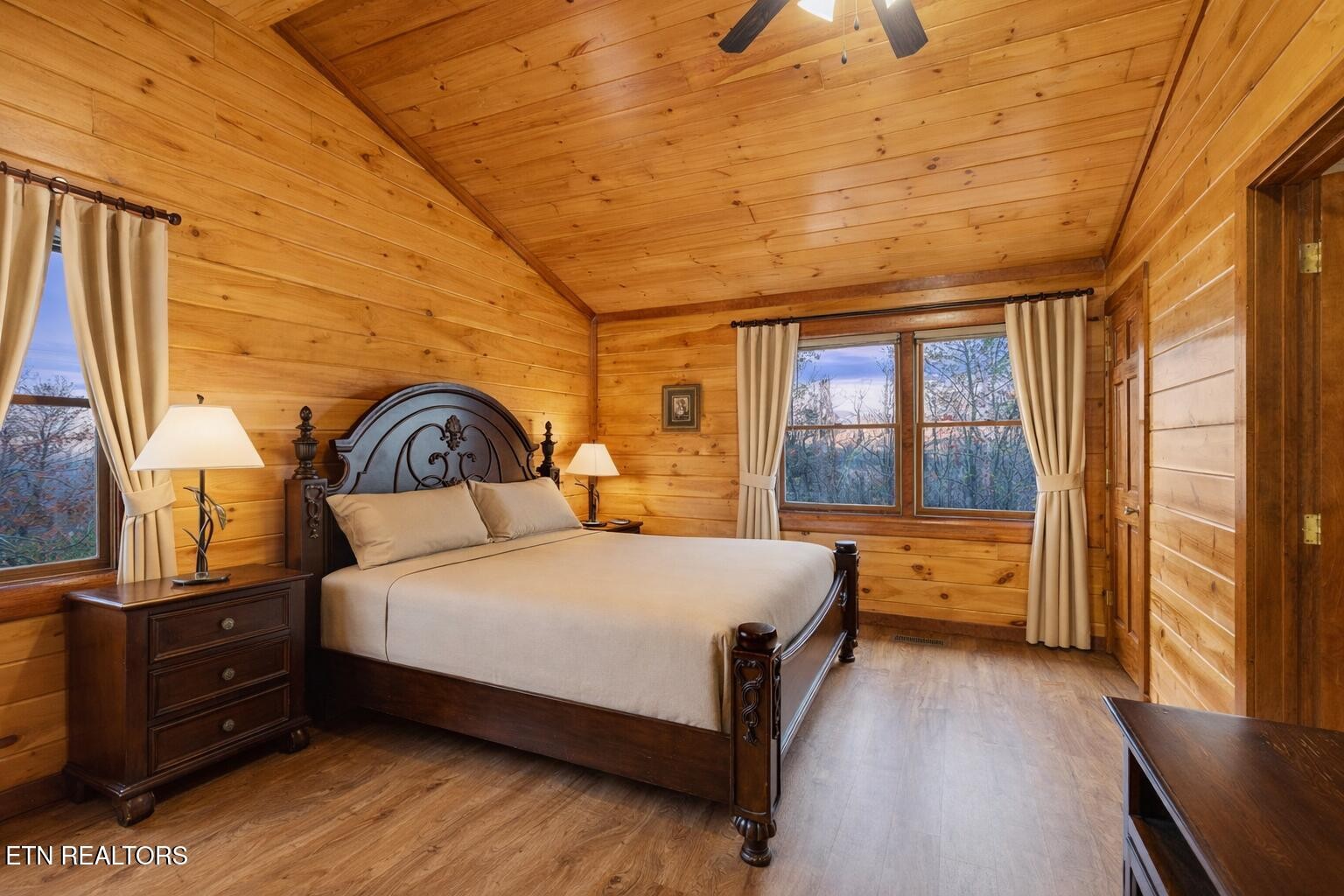 Wood-paneled cabin bedroom with a carved dark-wood bed beneath a vaulted pine ceiling.
