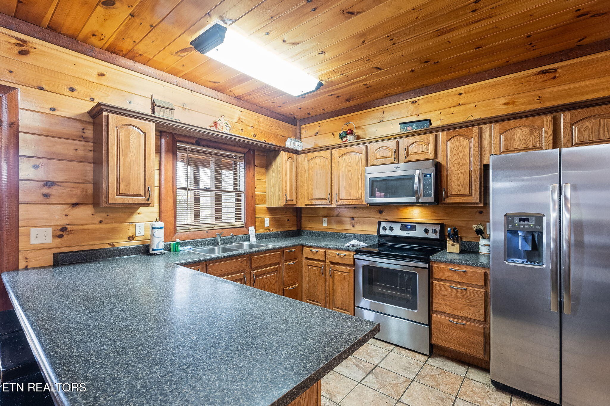 Kitchen with knotty wood walls, dark granite peninsula, and stainless steel appliances.