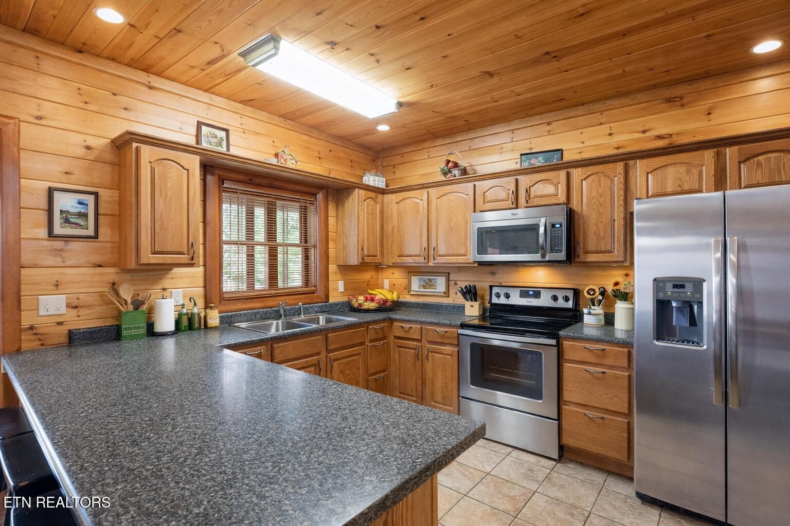 Wood-paneled kitchen with granite peninsula, stainless-steel appliances, and a window with blinds.