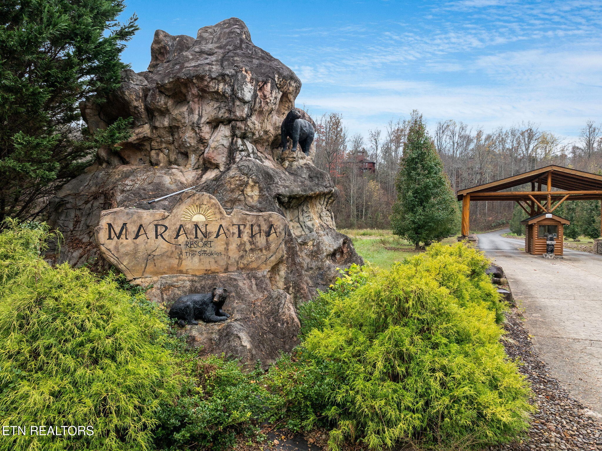 Maranatha Resort entrance sign beside a covered wooden drive, framed by landscaping and bear sculptures.