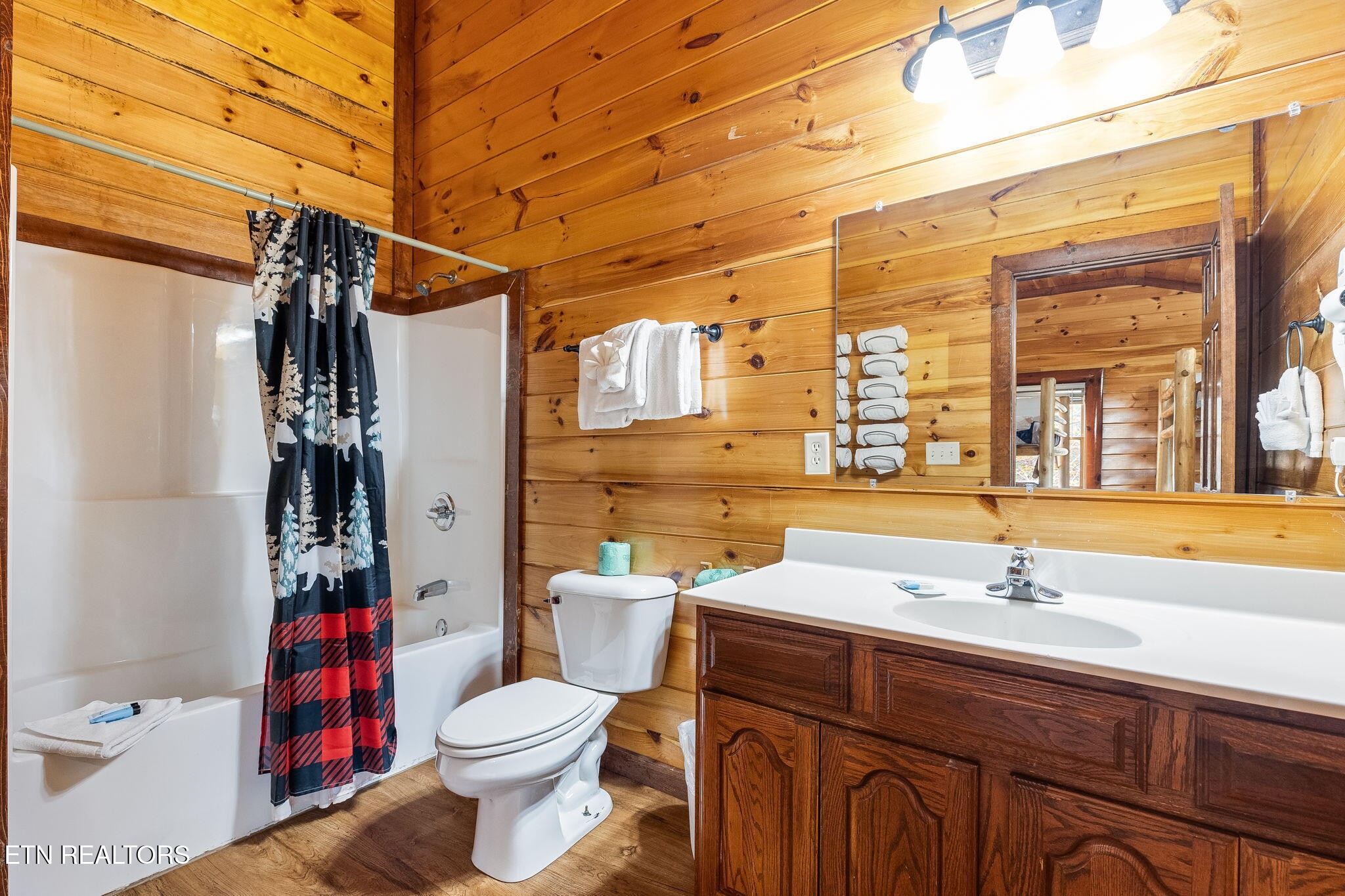 Cabin bathroom with wood-plank walls, a white tub and shower, and a dark wood vanity.