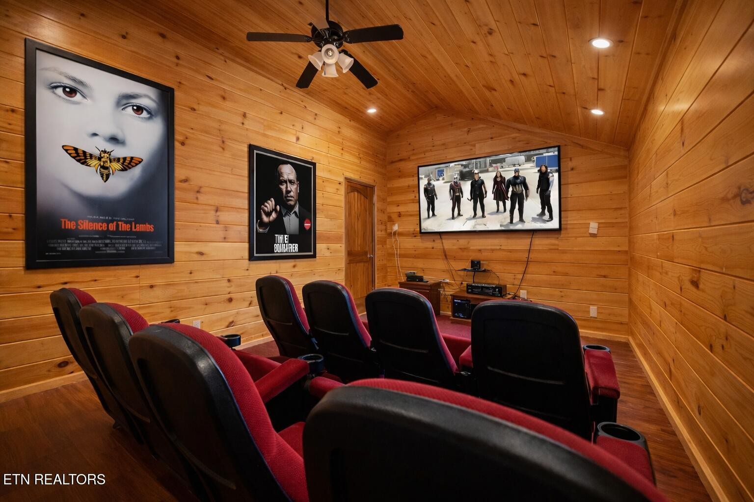 Home theater with red reclining seats, wood paneling, and movie posters.