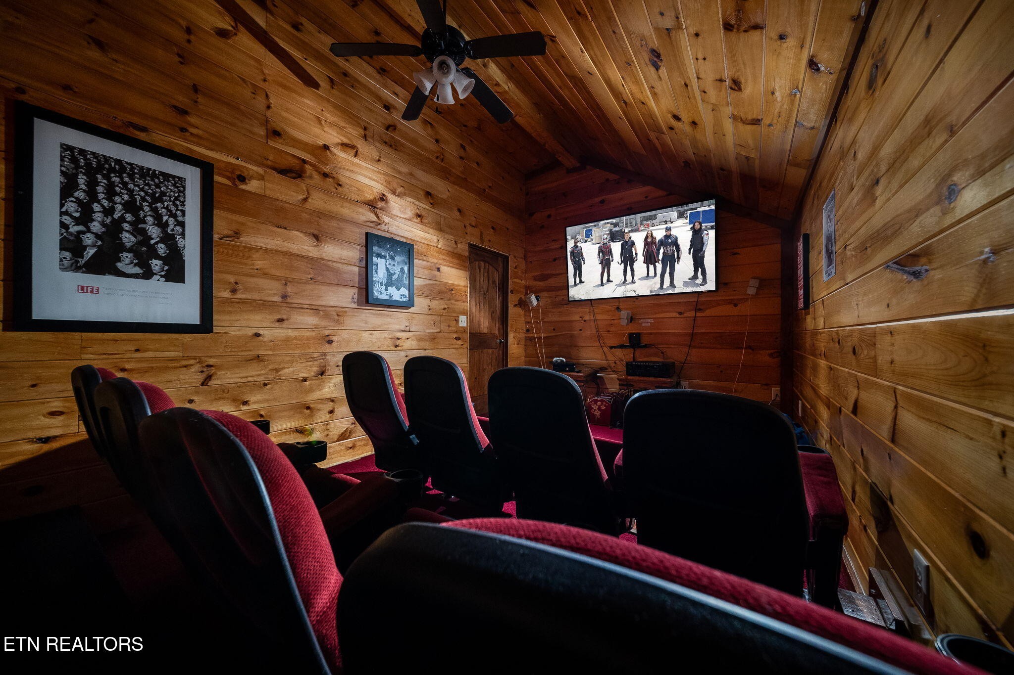 Wood-paneled home theater with red reclining seats and a wall-mounted television.