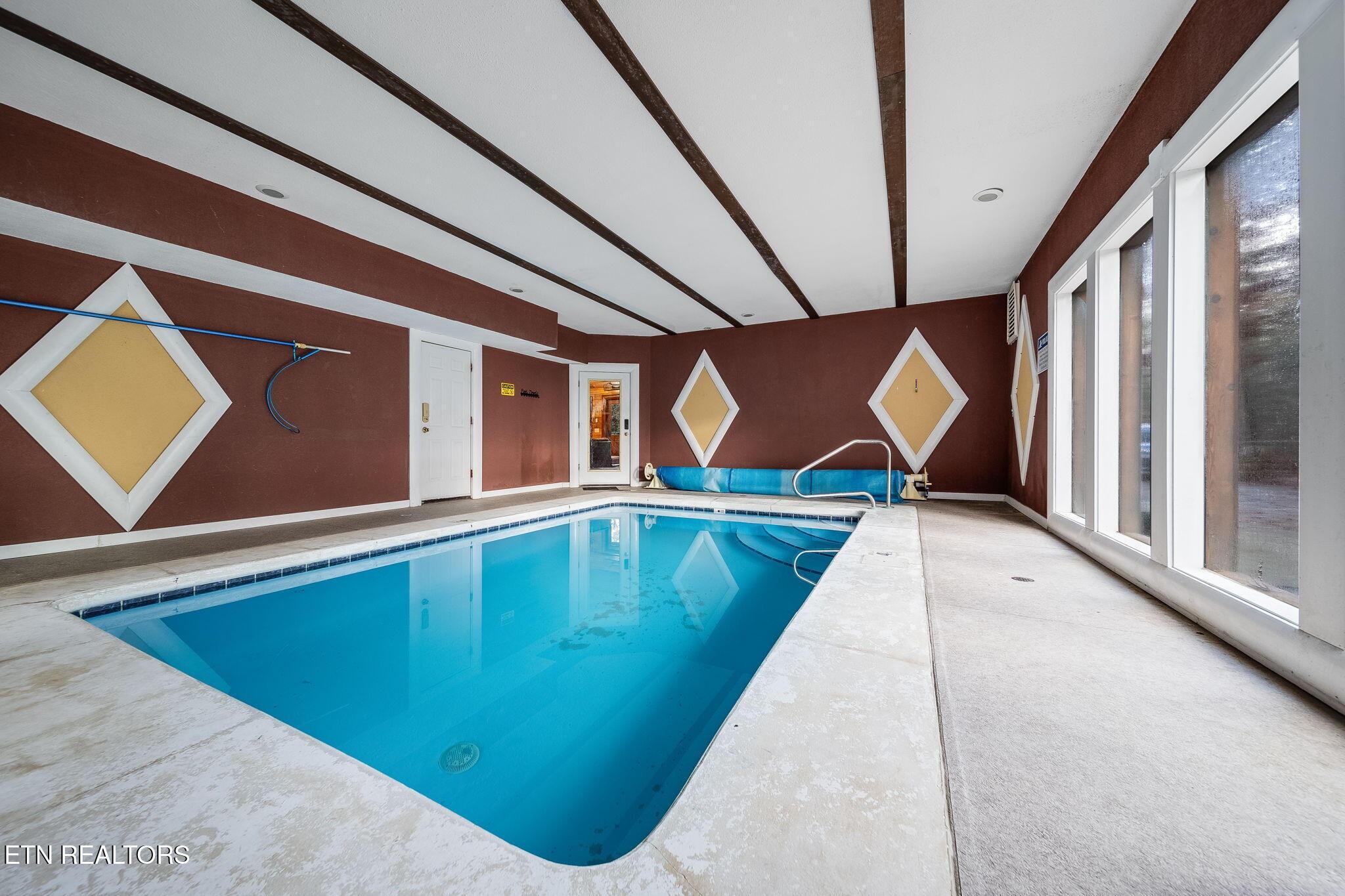 Indoor swimming pool with blue water, large windows, and decorative diamond wall panels.