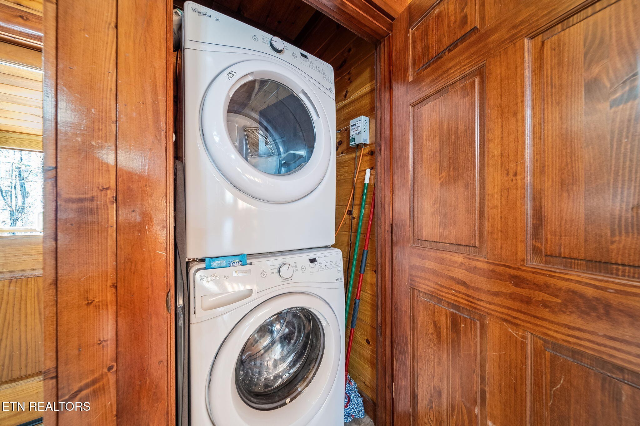 Stacked Whirlpool washer and dryer in a wood-paneled laundry closet.