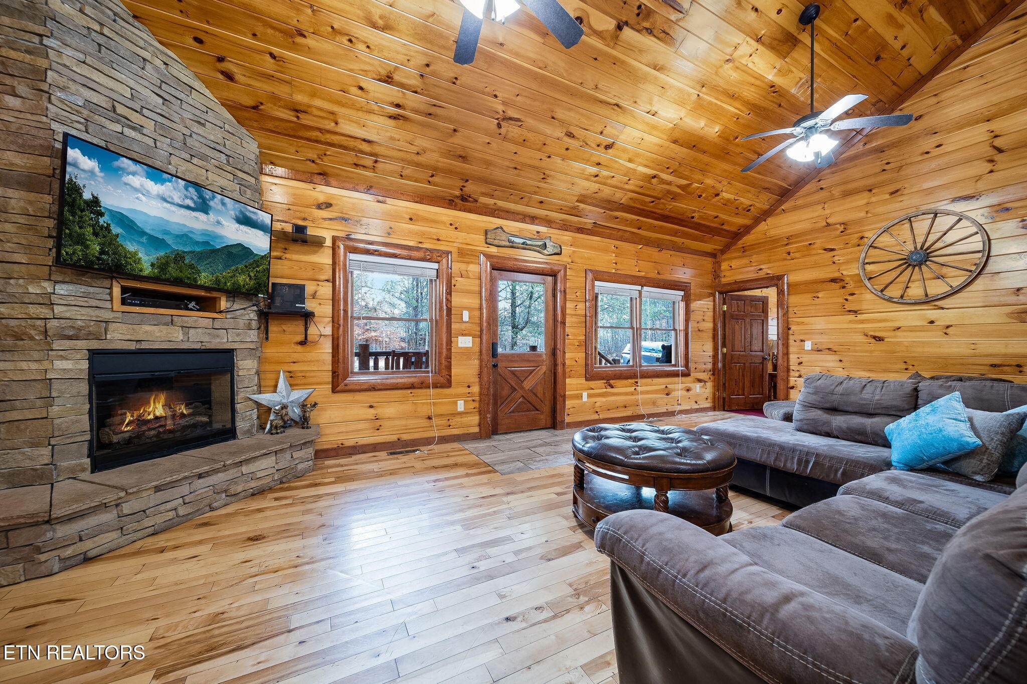 Cabin living room with a stone fireplace, vaulted wood ceiling, and gray sectional sofa.
