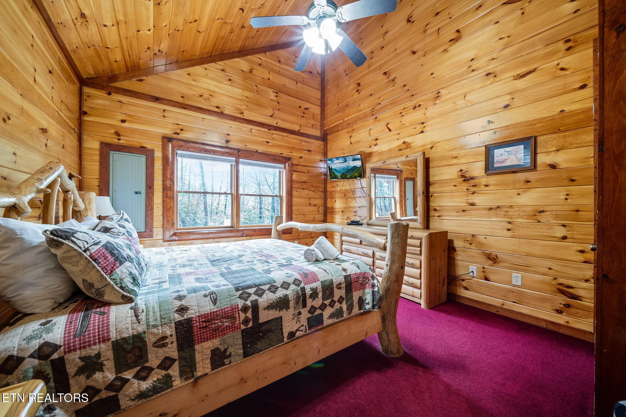 Cabin bedroom with a rustic log bed, patchwork quilt, and honey-colored wood walls.