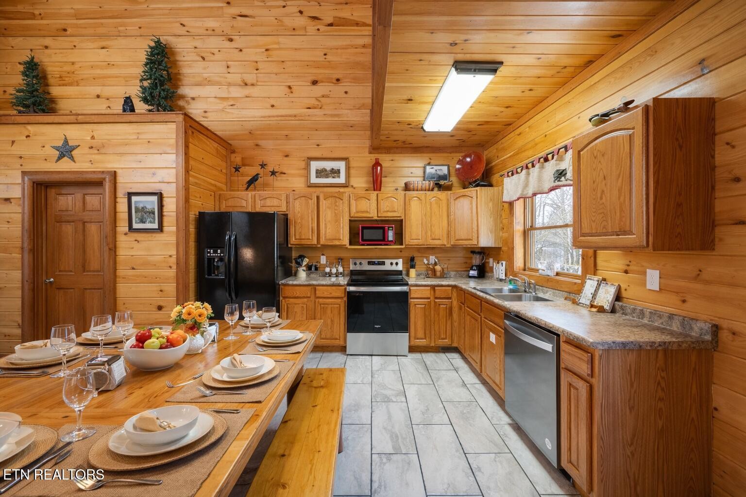 Wood-paneled kitchen with a set dining table, black appliances, and a sink beneath a window.