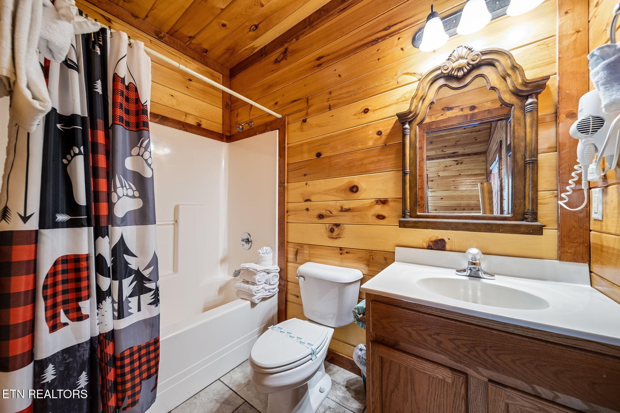 Cabin bathroom with wood-plank walls, a patterned shower curtain, and an ornate mirror above the vanity.