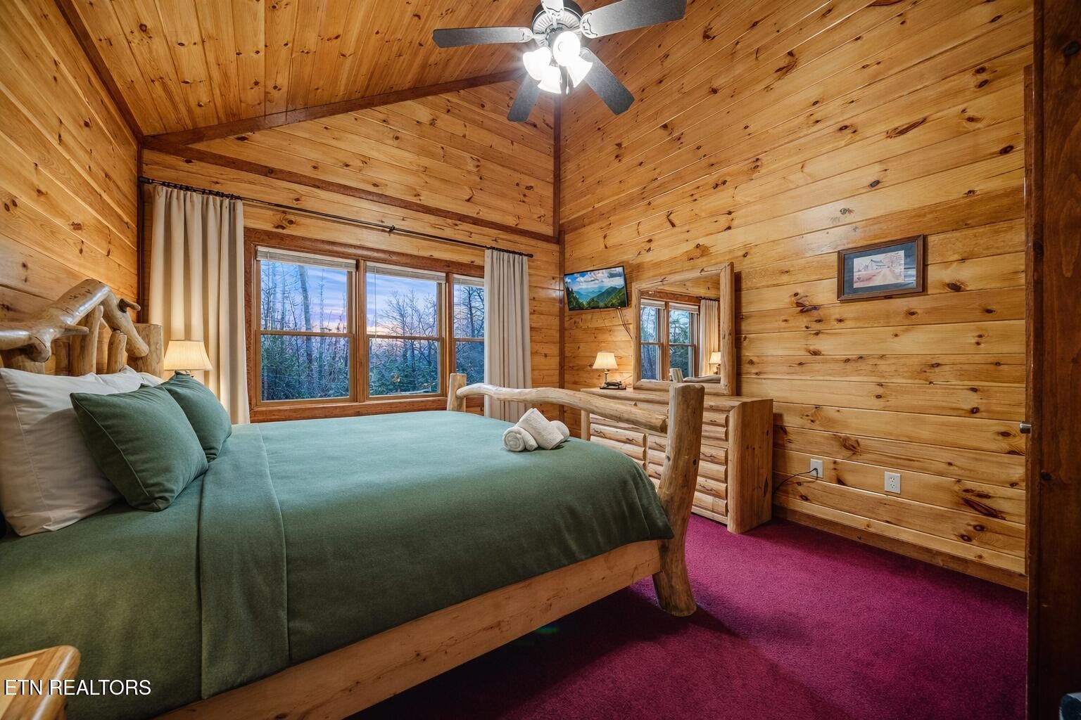 Cabin bedroom with green bedding, log-style furnishings, and a high wood-paneled ceiling.