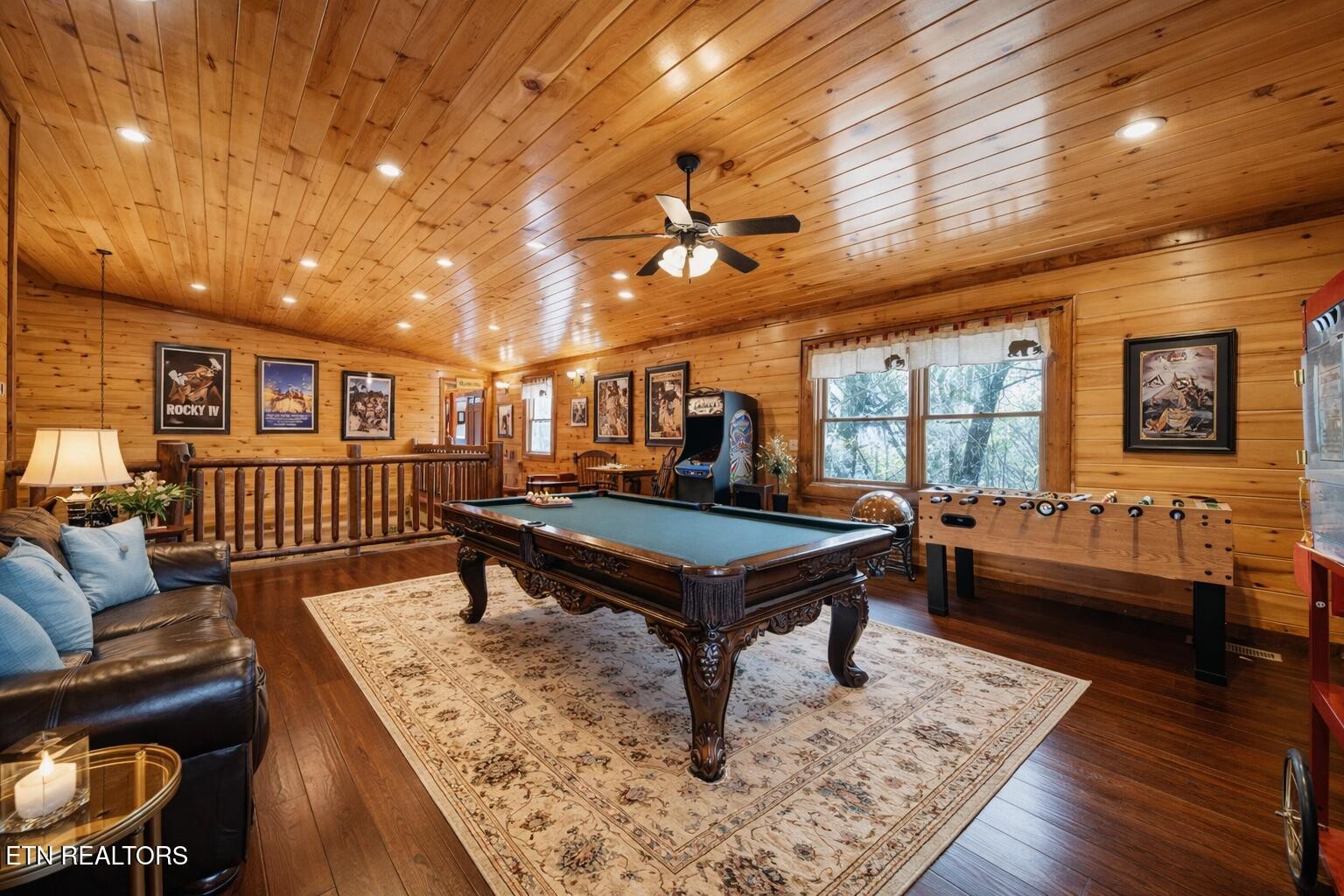 Wood-paneled game room with a pool table, foosball table, and leather seating.