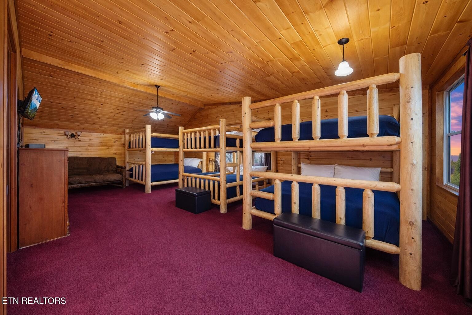 Cabin bunk room with log-frame beds, blue bedding, wood paneling, and burgundy carpet.