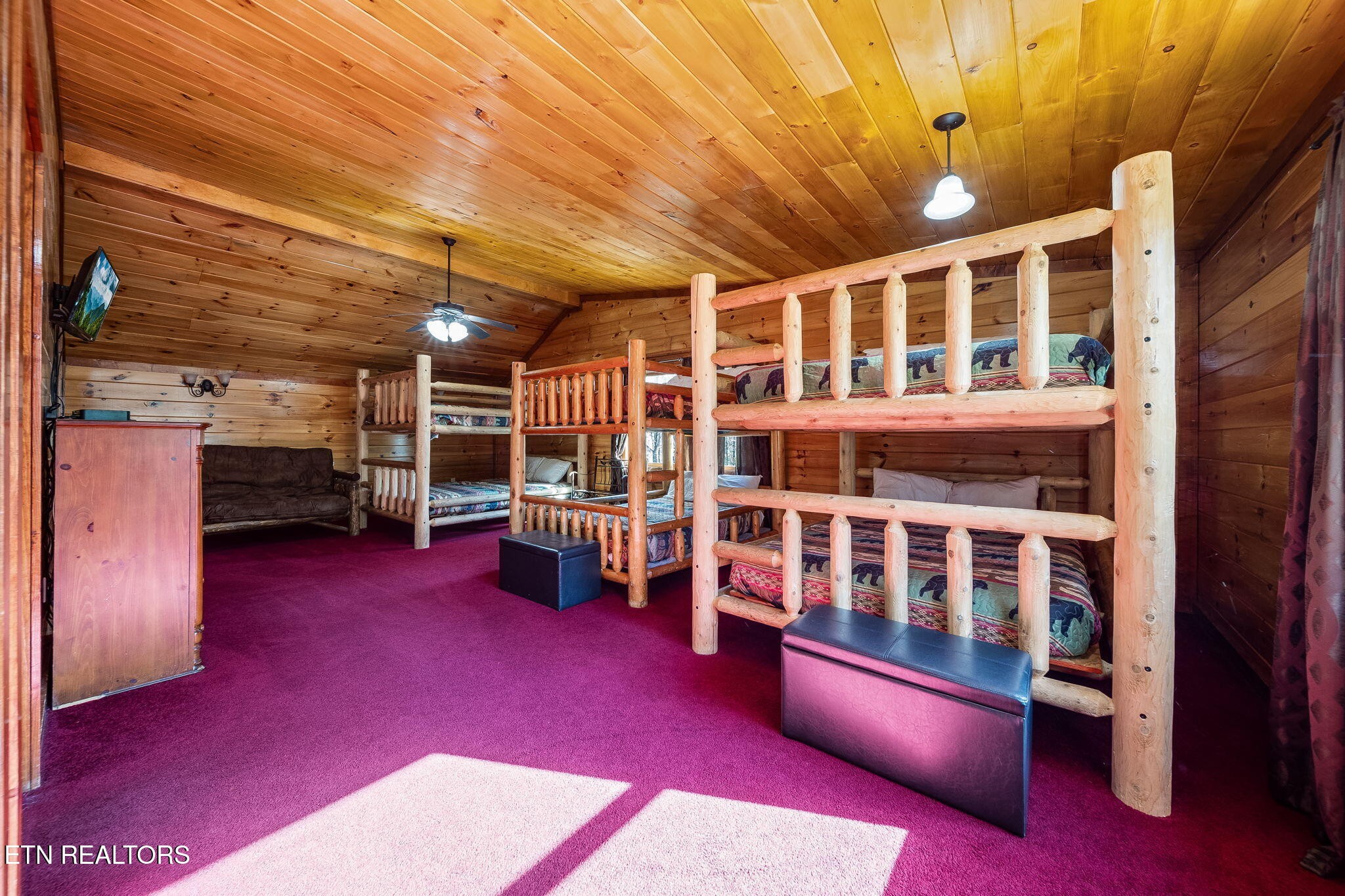 Cabin bedroom with rustic log bunk beds, wood-paneled walls, and magenta carpet.