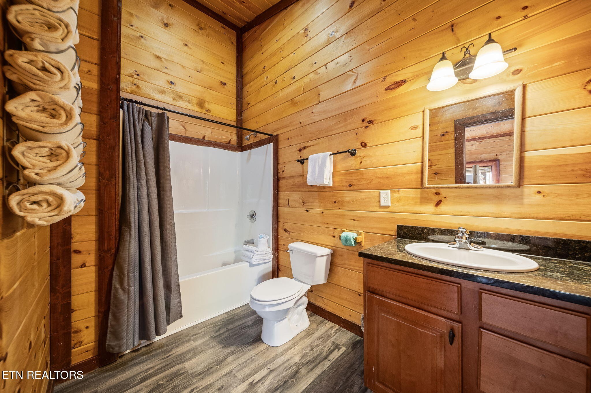 Cabin bathroom with knotty pine walls, a curtained tub and shower, and a wood vanity.