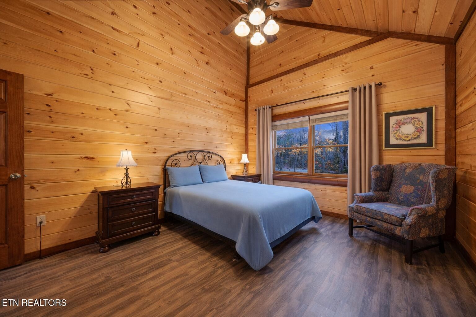 Bedroom with wood-plank walls, vaulted ceiling, metal-frame bed, and patterned armchair.