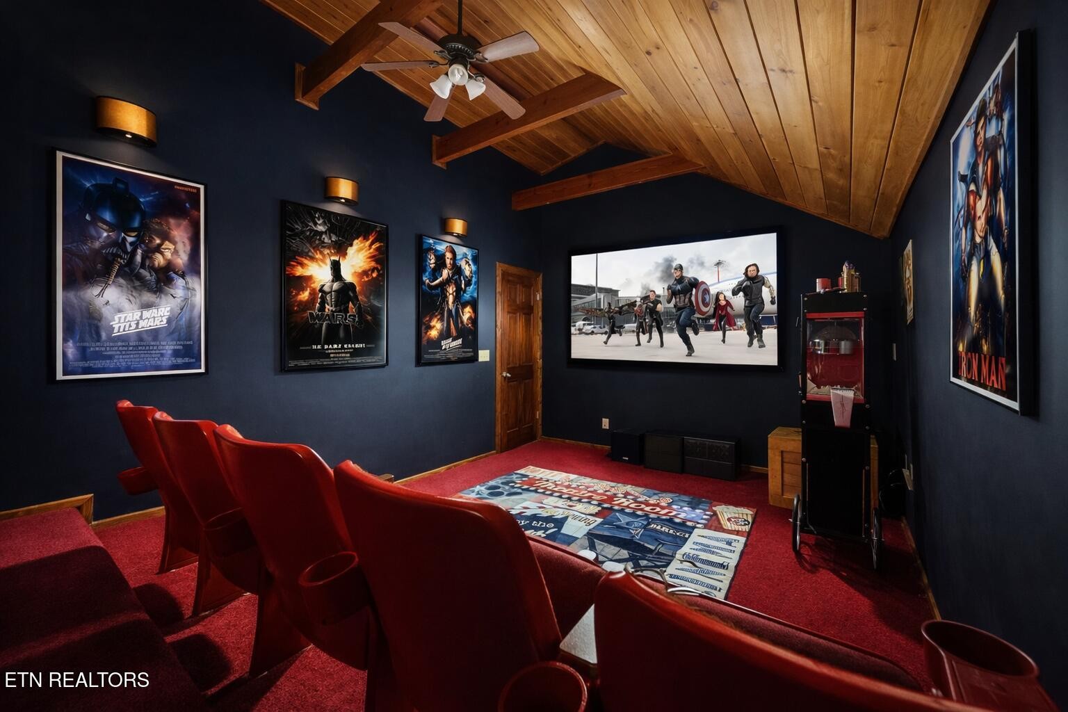 Home theater with red reclining seats, a large screen, movie posters, and a vaulted wood ceiling.